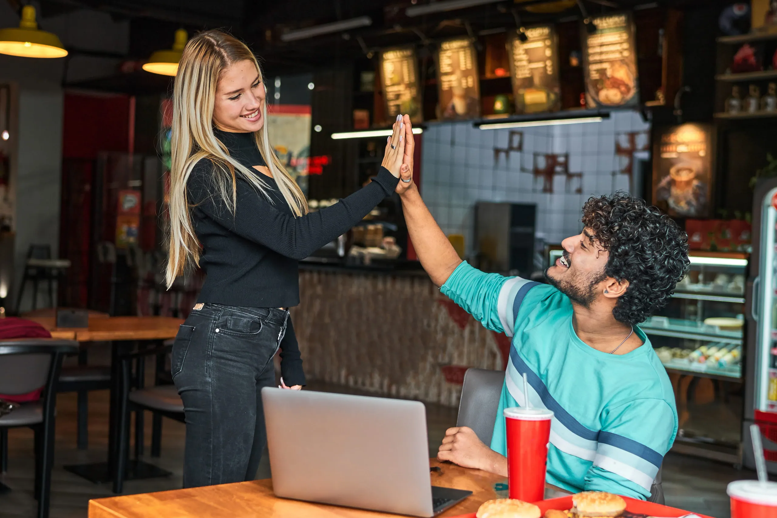 Two colleagues sharing a high five over a laptop in a café