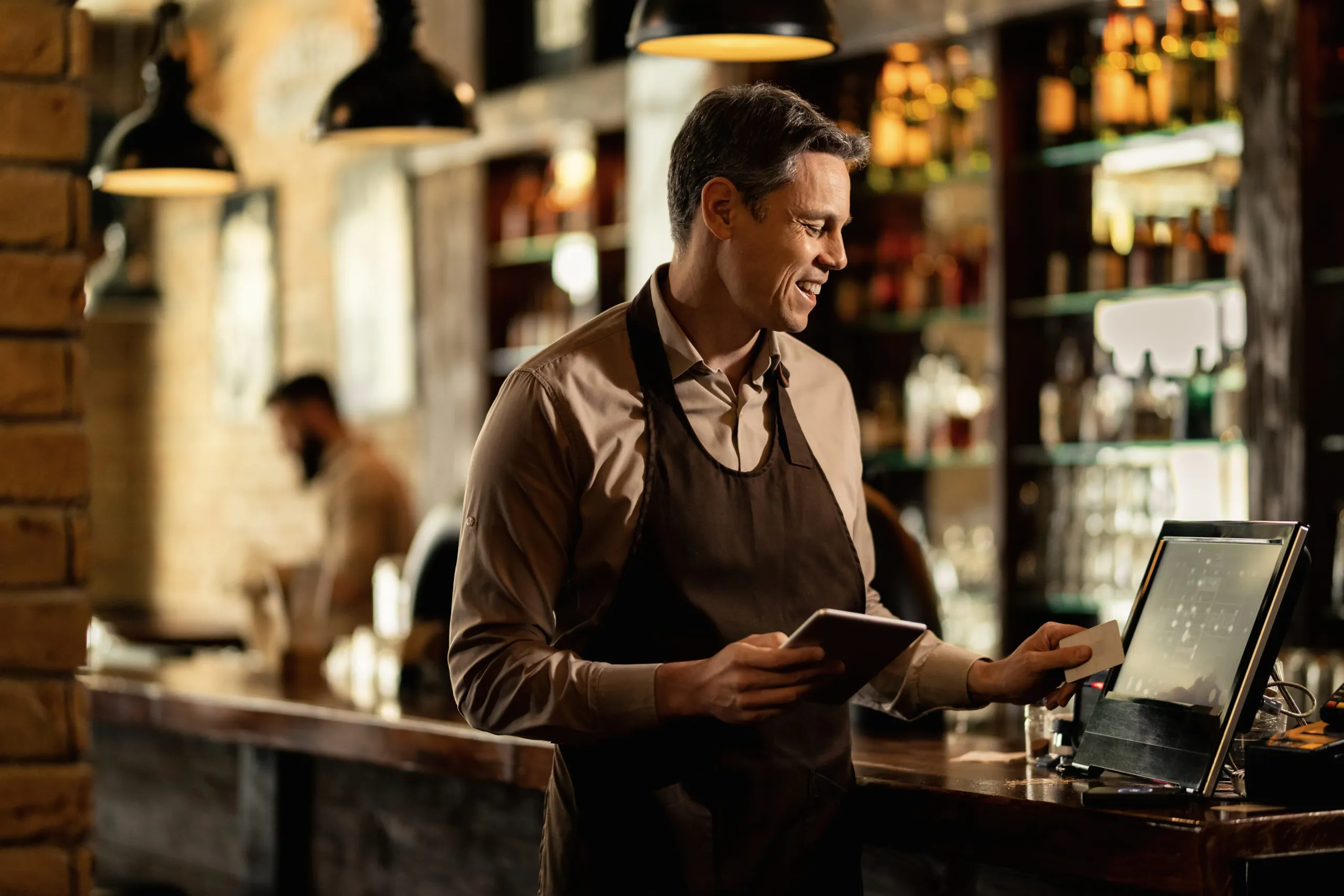 A bartender entering an order at the till while working behind a bar