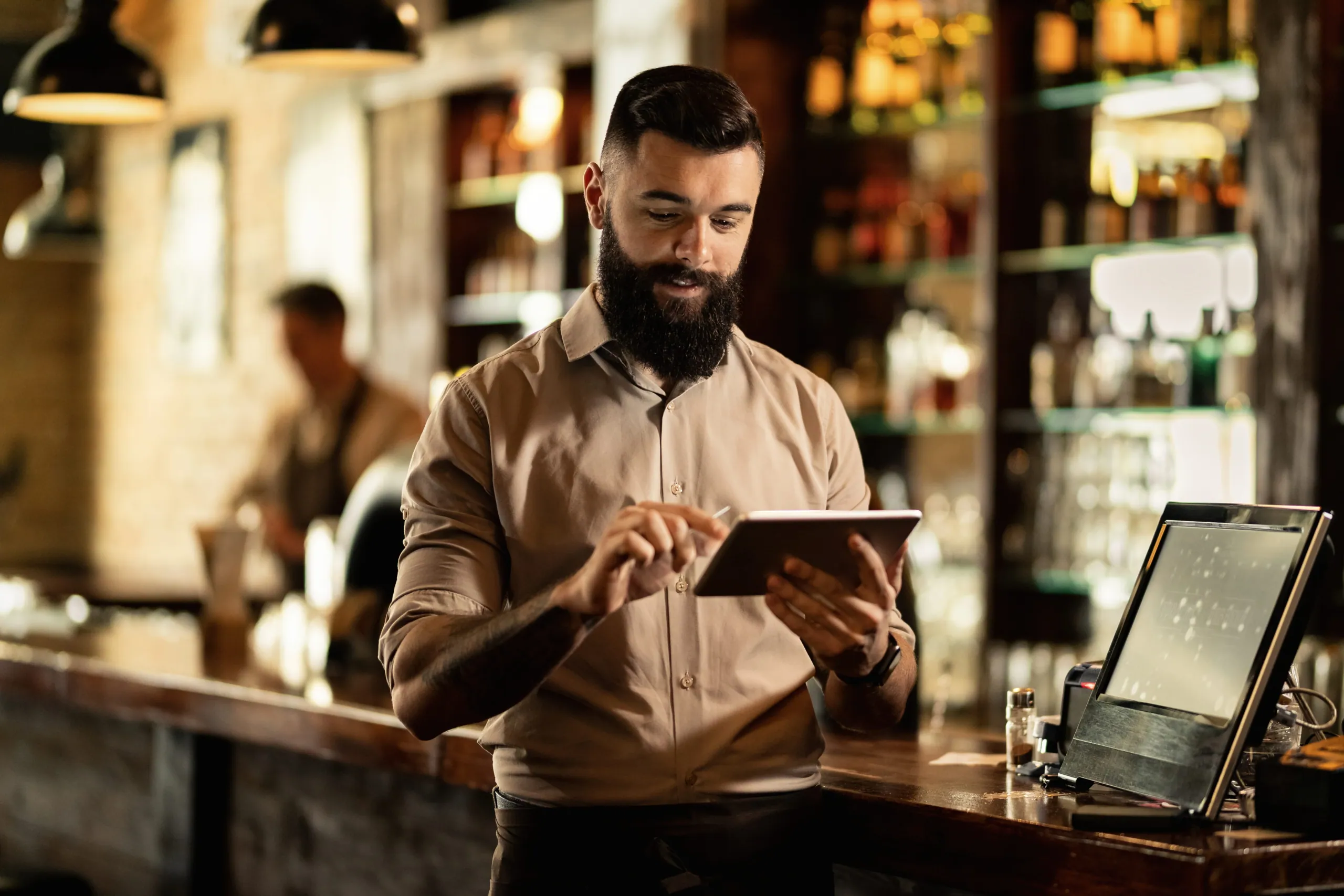 A barista checking a tablet while working behind a bar