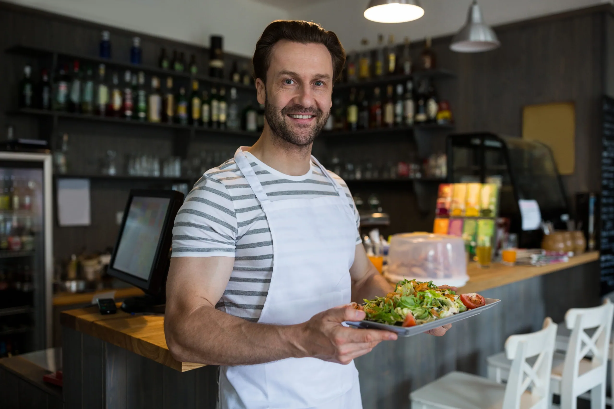 A waiter holding a plated salad in front of a restaurant bar